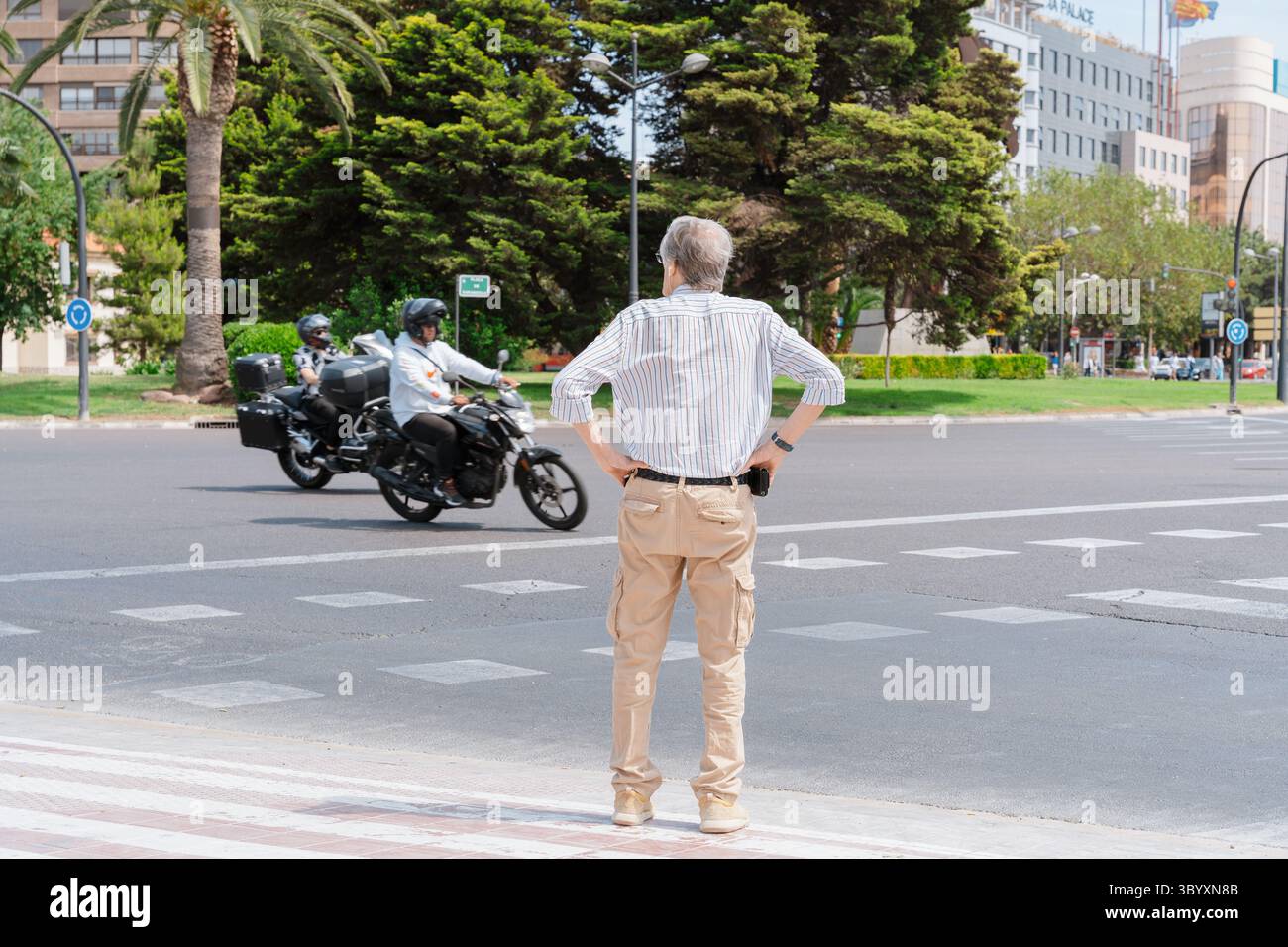 Valencia, Spain - May 06, 2023: Older man stands at pedestrian crossing while two motorbikes drive by on a multilane road in central Valencia, traffic Stock Photo