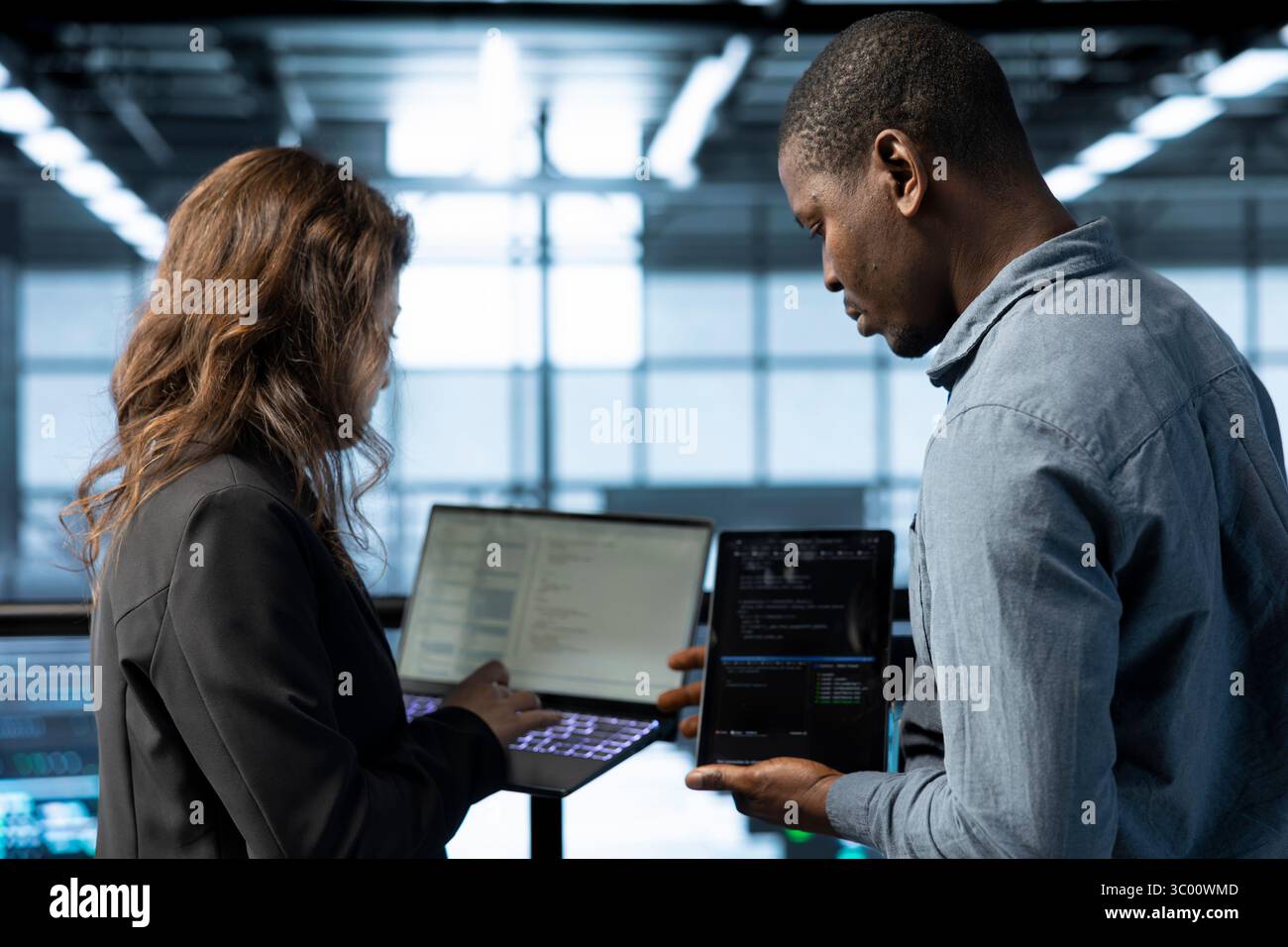 Software developers in data center automating routine maintenance tasks with laptop, executing diagnostic scripts. Server hub IT professionals coding on notebook, adjusting power settings Stock Photo