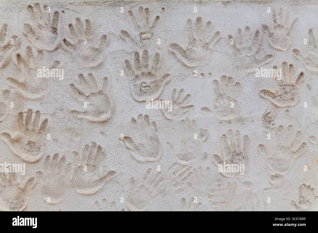 A textured wall features an array of handprints, creating a tactile and ...