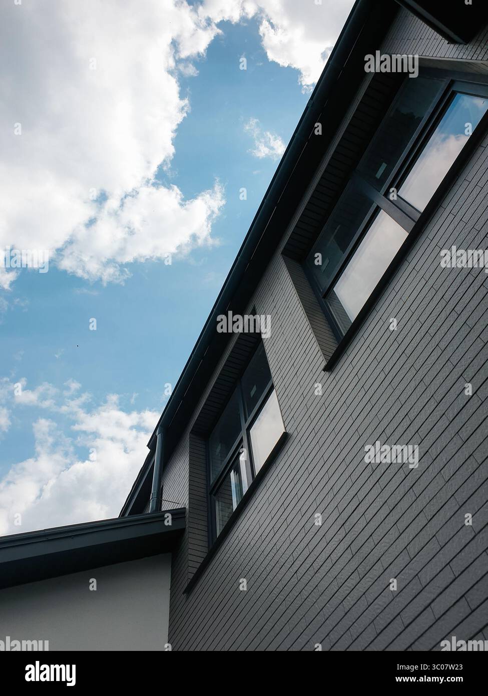 Windows under the roof on last floor of the building. Looking up at the grey brick building and clear blue sky in the background. Stock Photo