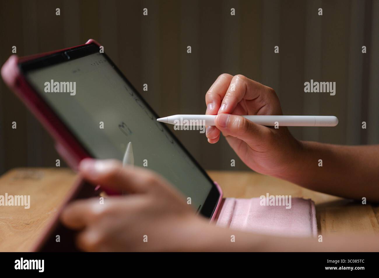 Cute Asian girl drawing using electronic tablet and stylus pen. Asian elementary school girl using digital tablet sitting in living room at home. Stock Photo