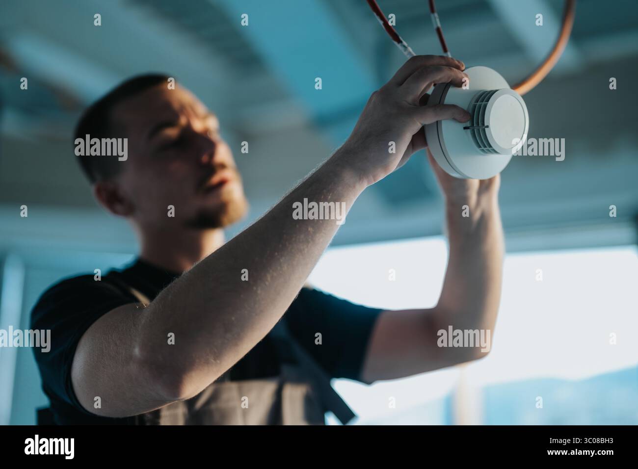 Technician installing a ceiling-mounted smoke detector device in a modern setting. Stock Photo