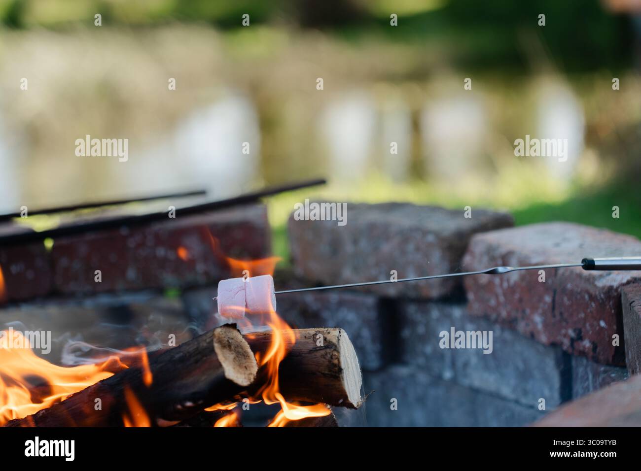 Roasting marshmallows at a lakeside brick fire pit at sunset Stock Photo