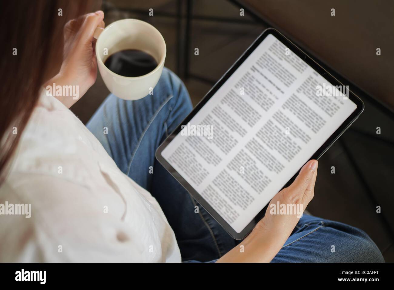 woman hand holding coffee cup and tablet, reading text on tablet device with a touchscreen interface for digital press article feed in the morning. Stock Photo