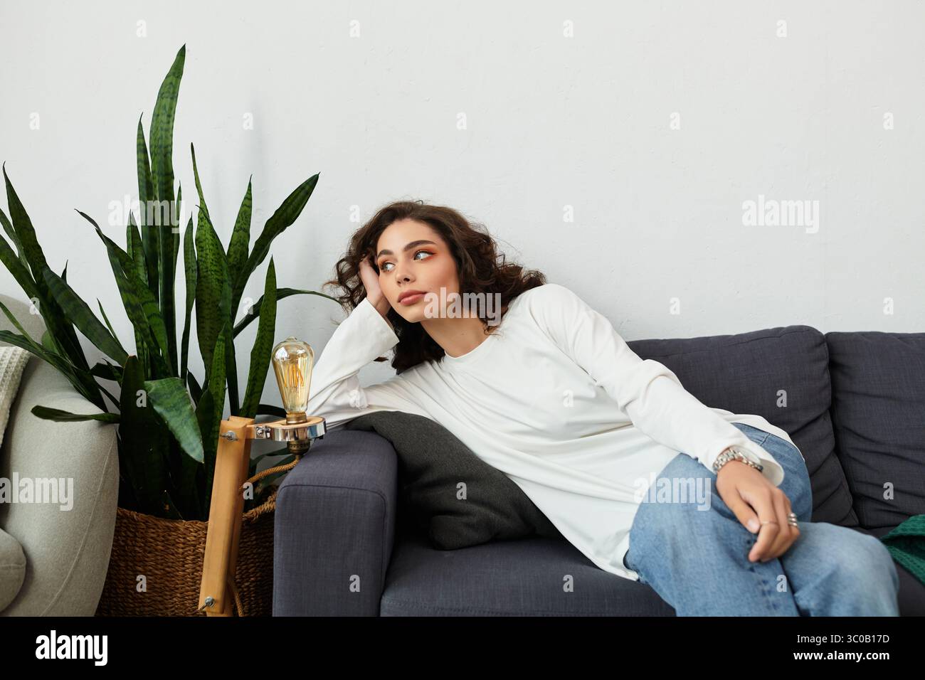 A young woman with curly brown hair relaxes on a couch in her cozy ...