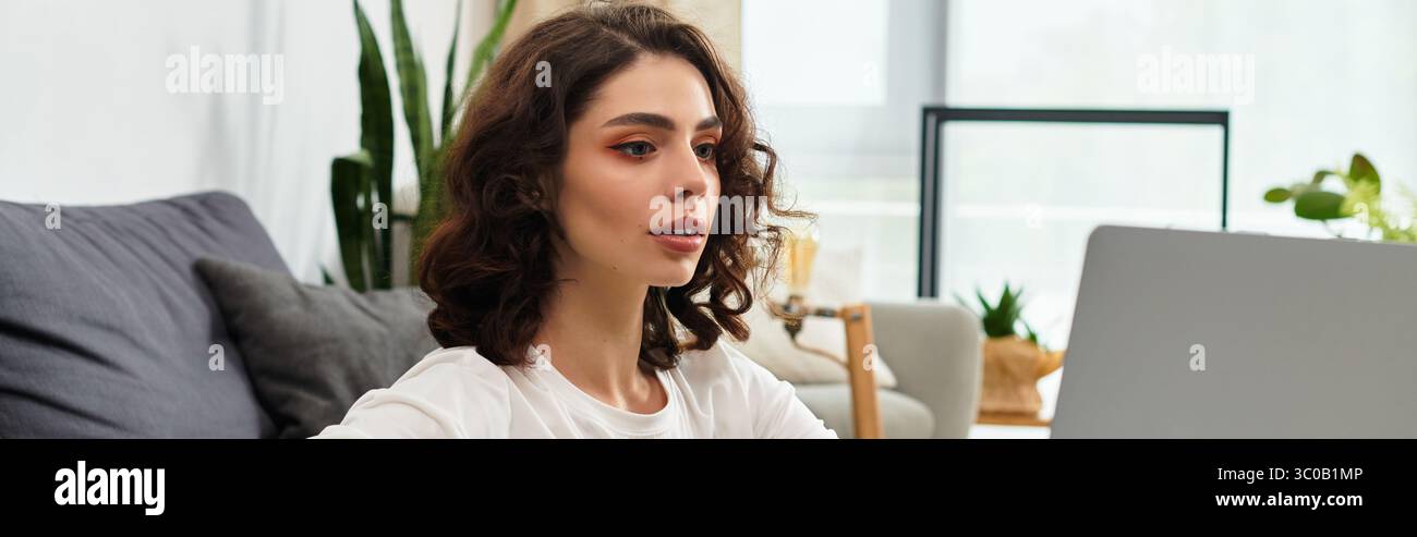 A young woman with curly hair focuses intently on her laptop in a ...