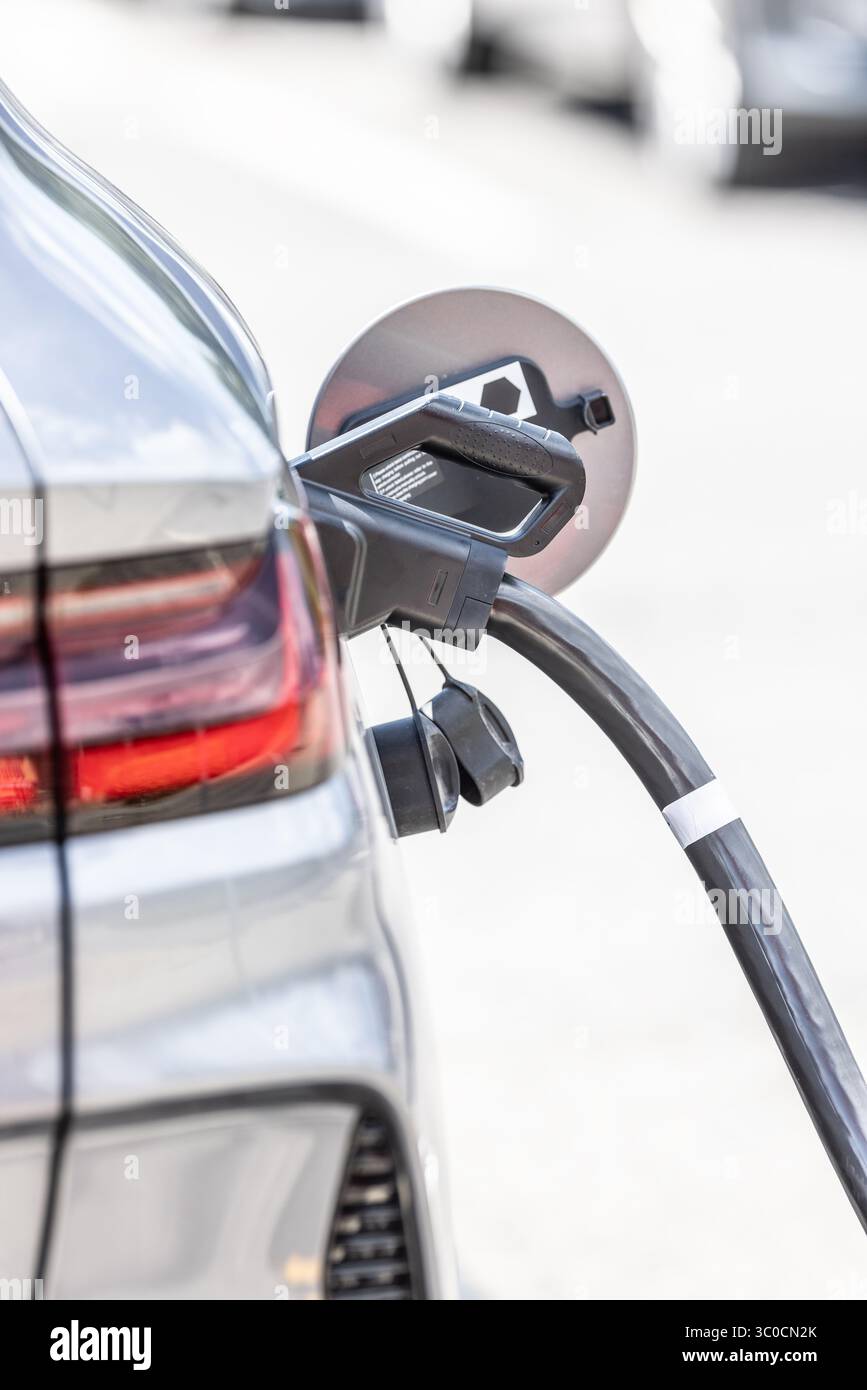 Focus closeup electric vehicle plugged in with EV charger device from blurred background of public charging station powered by renewable clean energy Stock Photo