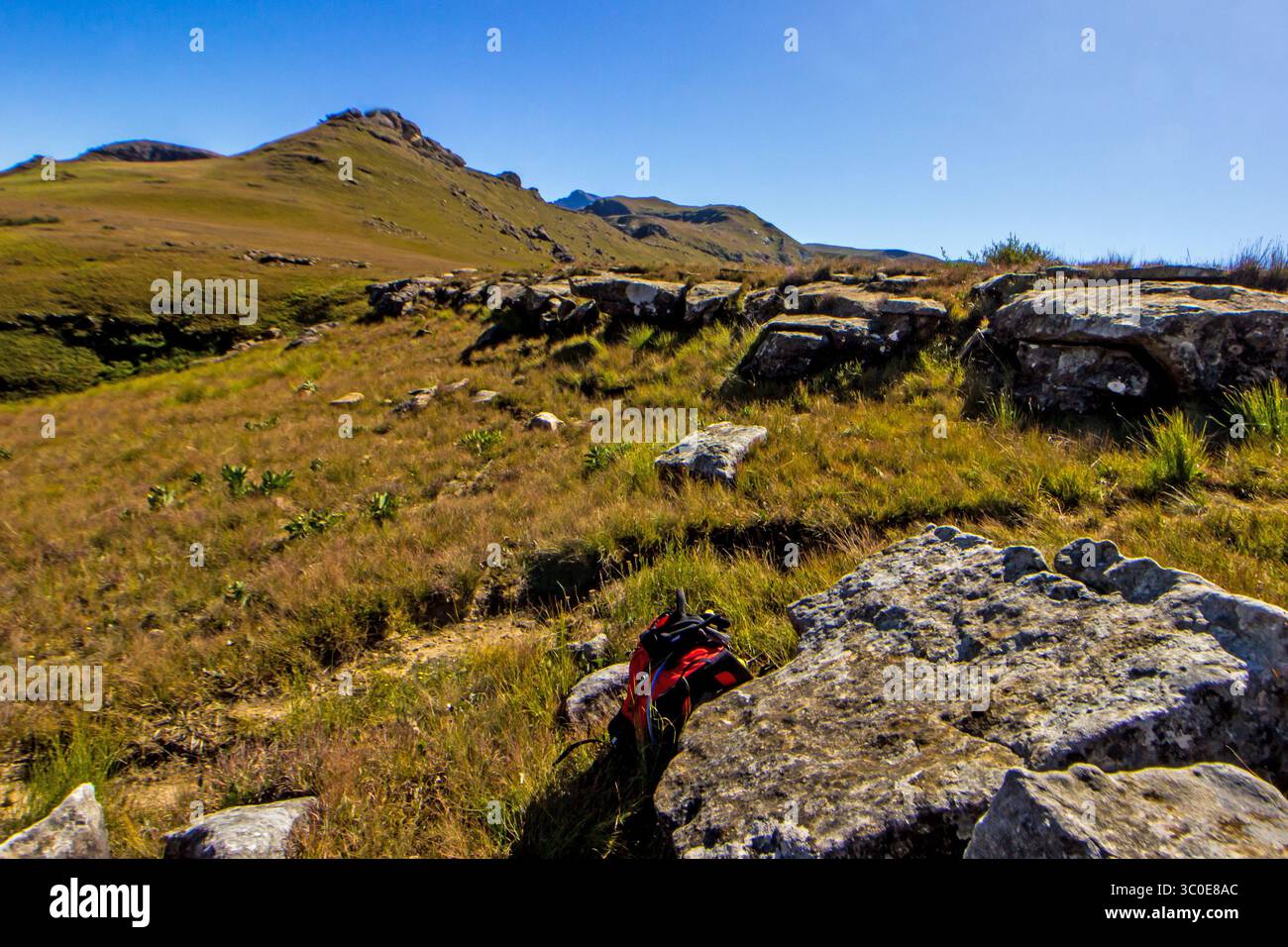 A small red backpack next to a hiking trail in the remote high altitude sections of the Central Drakensberg mountains in South Africa Stock Photo