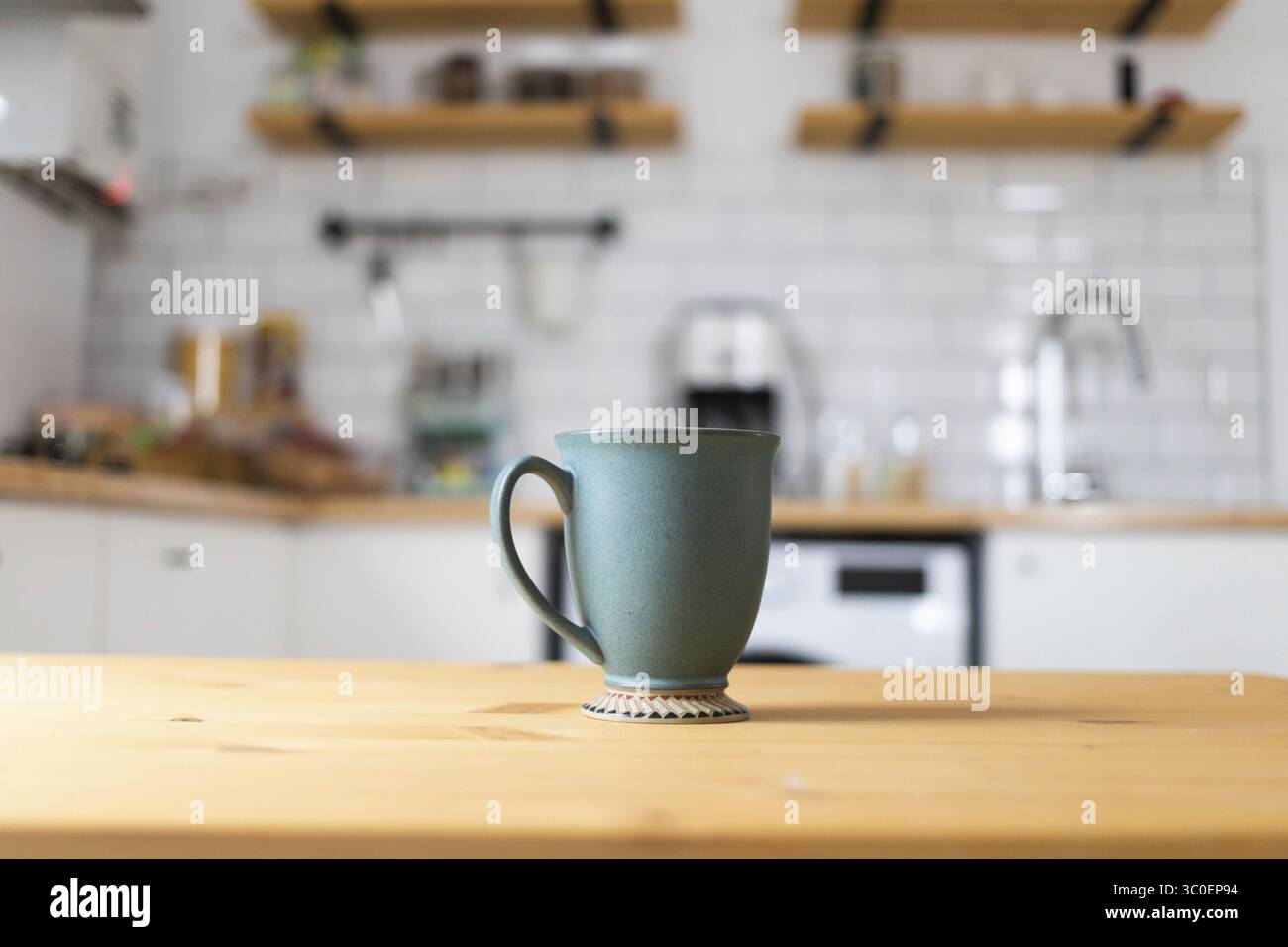 Green coffee cup on kitchen table blurred kitchen in background Stock Photo