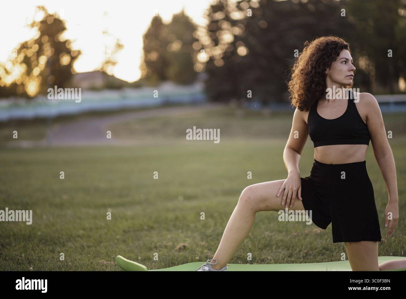 Woman stretching her leg on a mat in a park during the evening Stock Photo