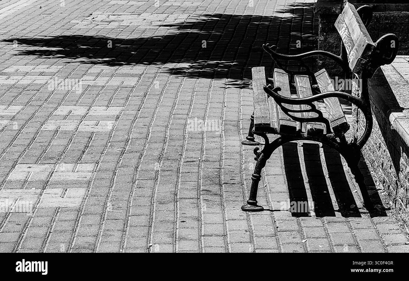 Midday Bench: Light and Shadow on a Hot Summer Sidewalk. City Street , pavement. Monochrome Hues. Stock Photo