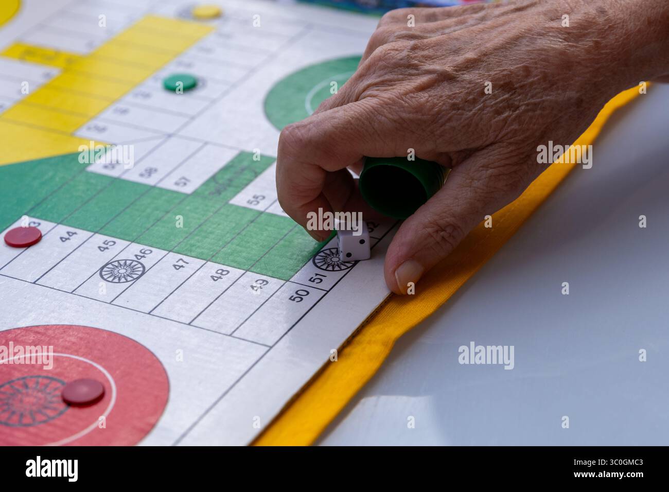 Wrinkled hand rolling dice onto a parcheesi board during an engaging game, showcasing leisure activity and entertainment Stock Photo