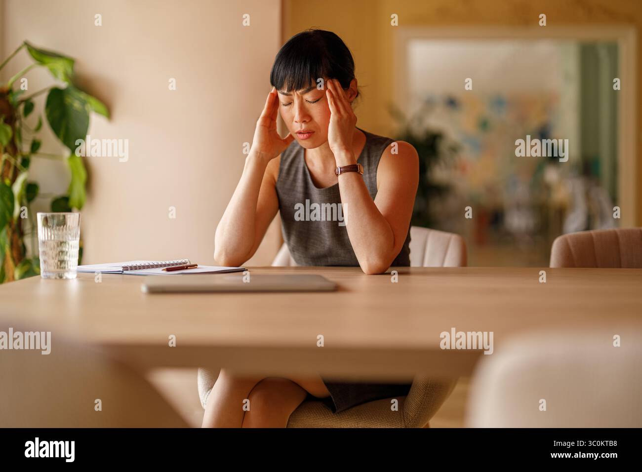 Stressed businesswoman with head in hands overwhelmed by workload and deadlines at corporate office desk Stock Photo