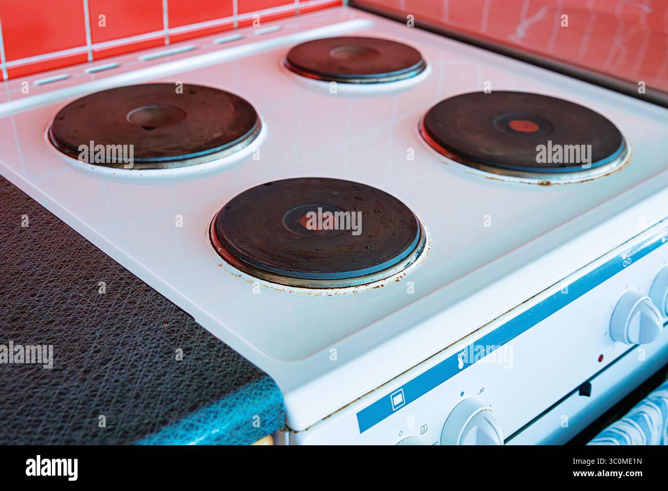 White electric stove with four black round hotplates in a domestic kitchen. the stove is clean and surrounded by a red tile backsplash Stock Photo