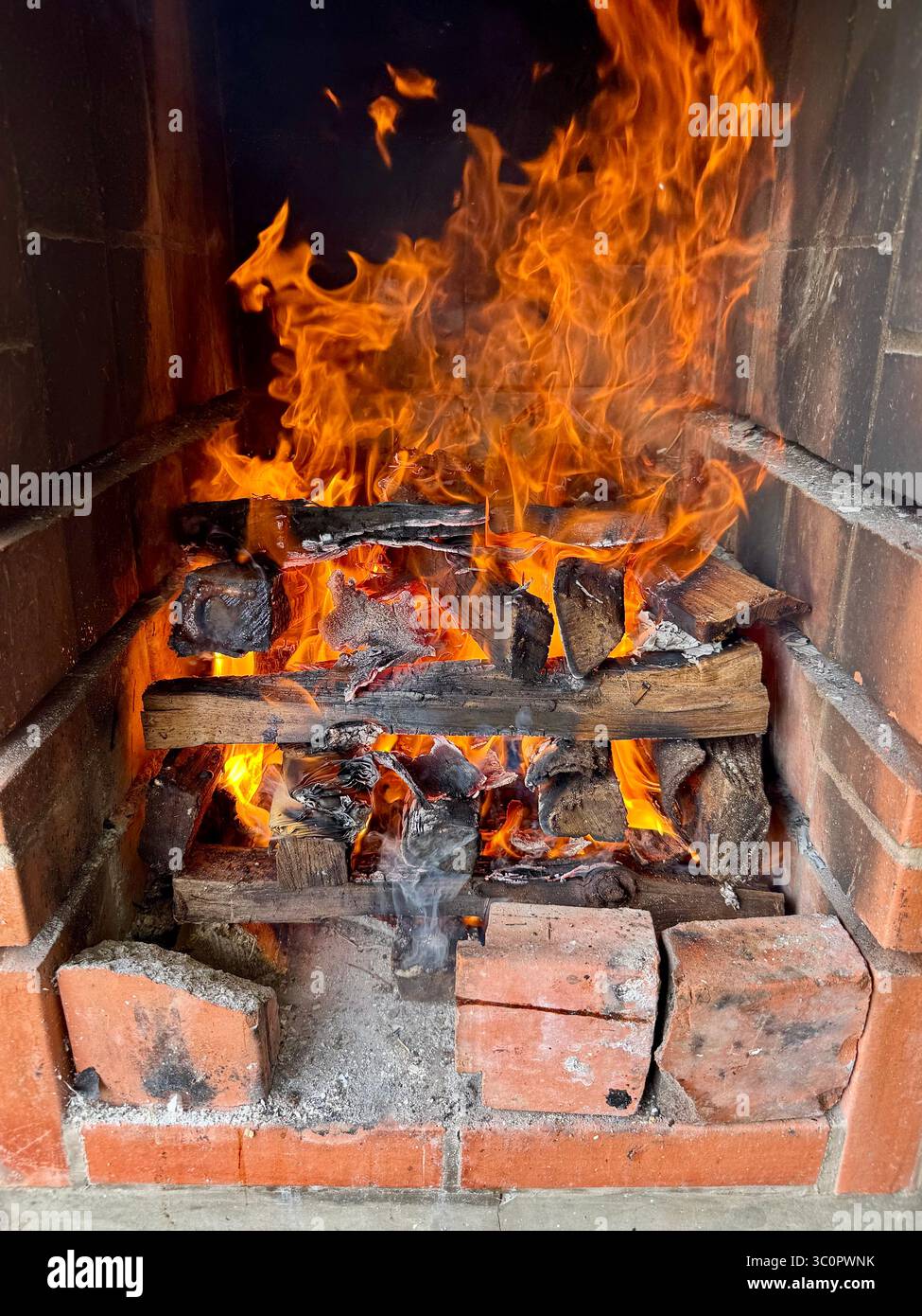 Flames and glowing embers in a brick fireplace with burning wood logs for barbecue - Smartphone Captured Stock Image
