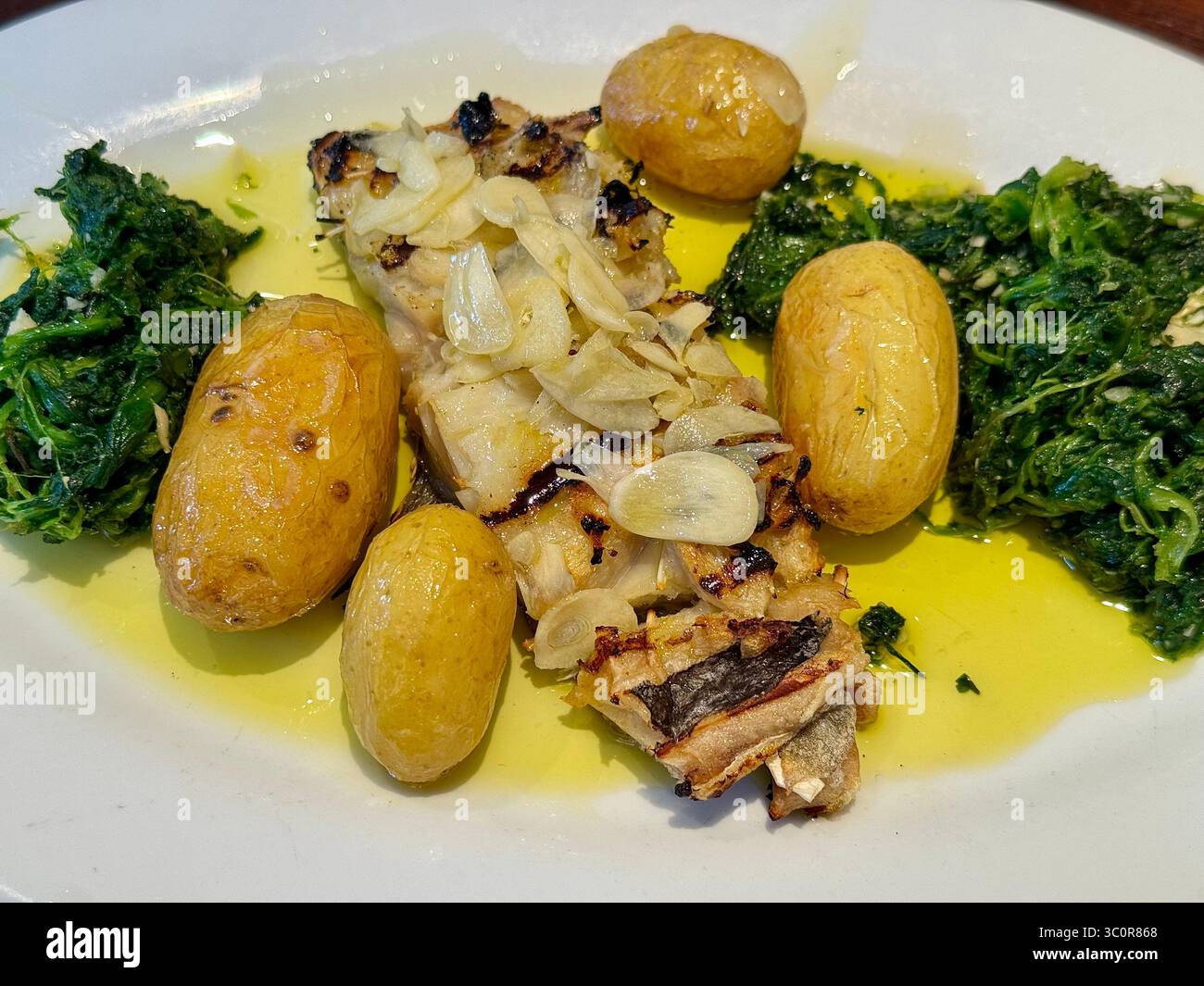 Traditional Portuguese bacalhau dish served with garlic, potatoes, and sautéed greens in olive oil. - Smartphone Captured Stock Image
