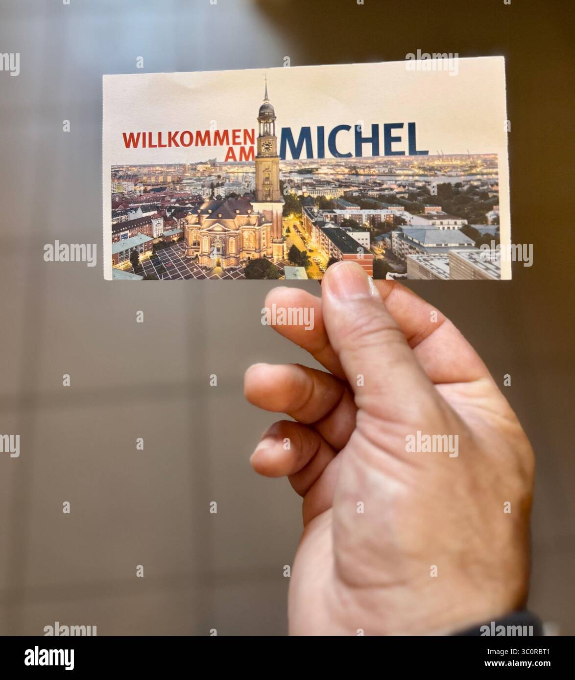 Hand holding an entrance ticket featuring “Willkommen am Michel,” referring to St. Michael’s Church in Hamburg, Germany. - Smartphone Captured Stock Image