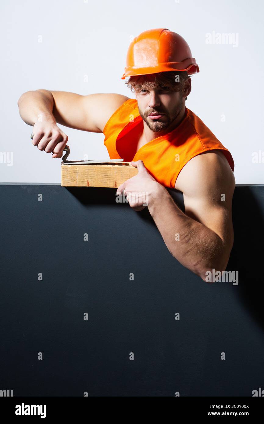 Builder with bricks, funny sale on construction site. Funny builder man with helmet doing brickwork. Builder posing with bricks blocks. Bricklayer Stock Photo