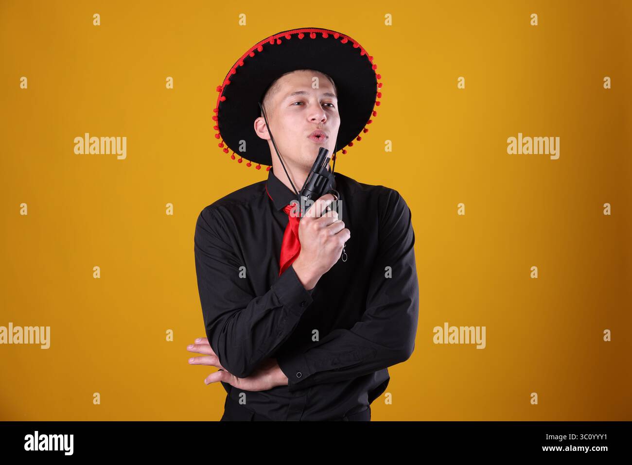 Man in black Flamenco hat with gun on yellow background Stock Photo