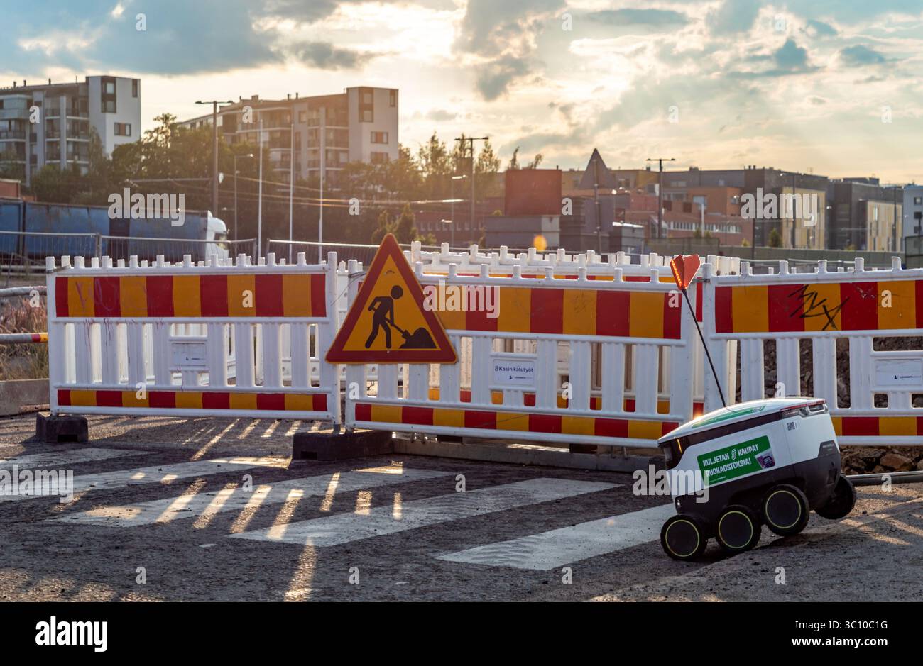 A Starship robot, delivering S Group groceries, negotiating Kyläsaarenkatu roadworks in light summer rain. Stock Photo