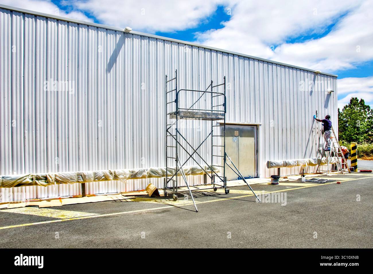 Contractors repainting the ribbed metal exterior walls of a warehouse - Chatellerault, Vienne (86), France. Stock Photo