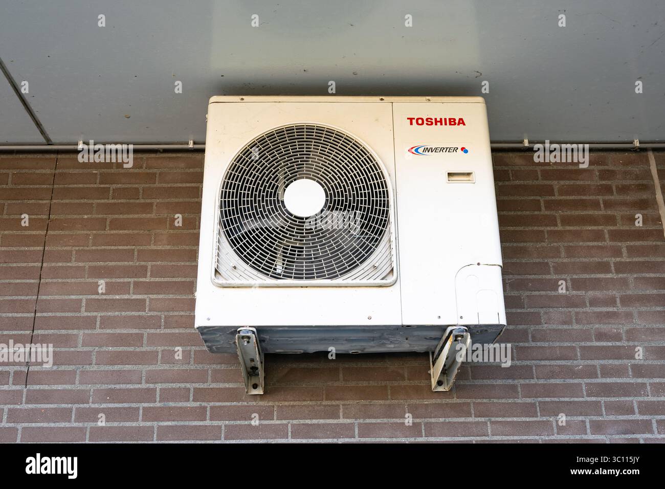 A white outdoor air conditioning unit mounted on a brick wall for ...