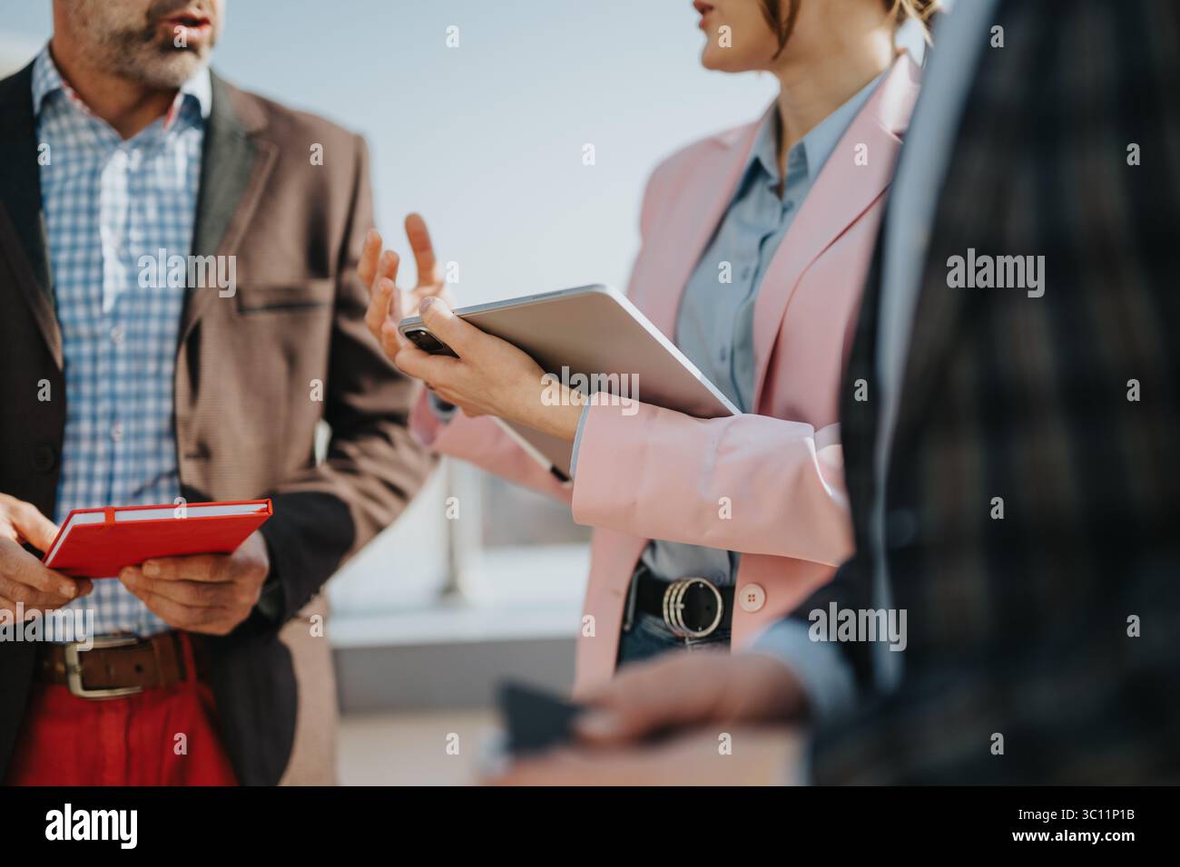 Team members having a discussion while reviewing notes and a tablet outdoors Stock Photo