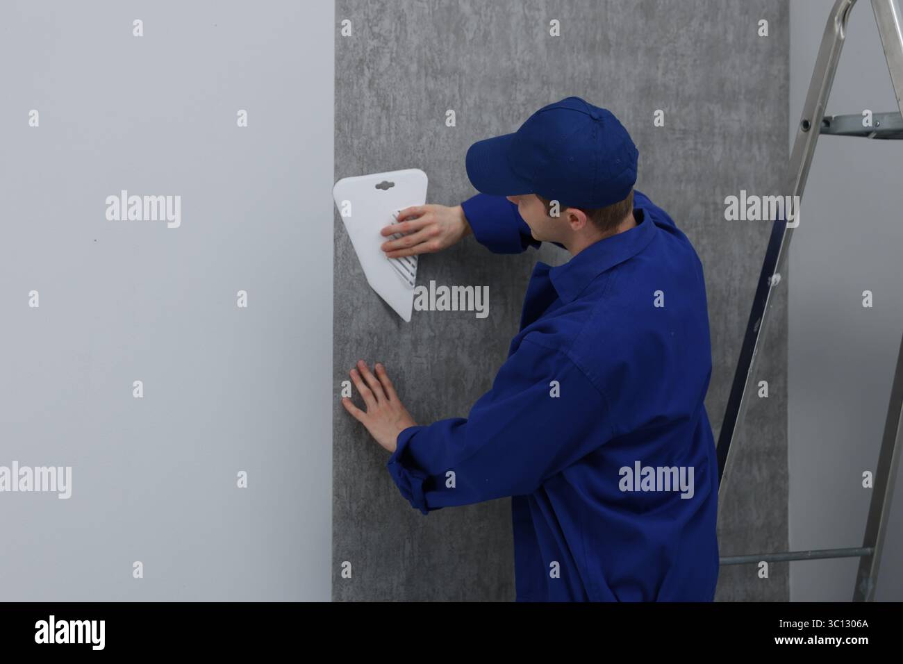 Worker smoothing wallpaper with tool in room Stock Photo