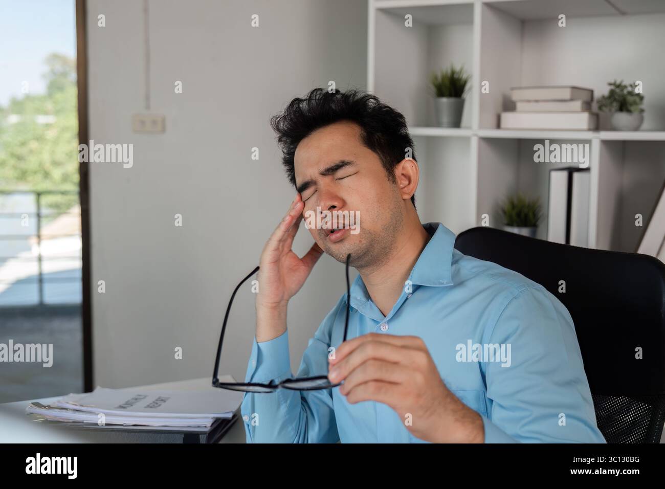 Exhausted Office Worker Experiencing Headache from Intense Workload in Modern Workplace Setting Stock Photo