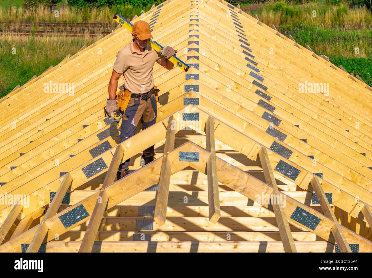 A construction worker uses a level tool on top of a wooden roof ...