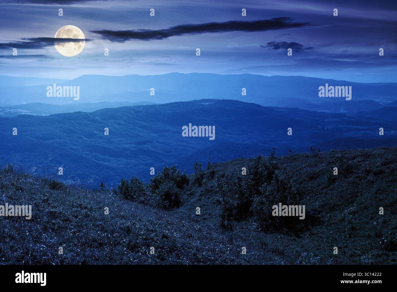 mountain landscape in summer at night. beautiful view of rolling green hills and alpine meadows in full moon light. scenery with clouds on the dark sk Stock Photo