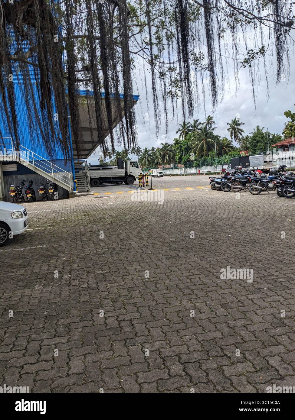 Motorcycles and vehicles parked near a blue warehouse building with palm trees in the background. - Smartphone Captured Stock Image