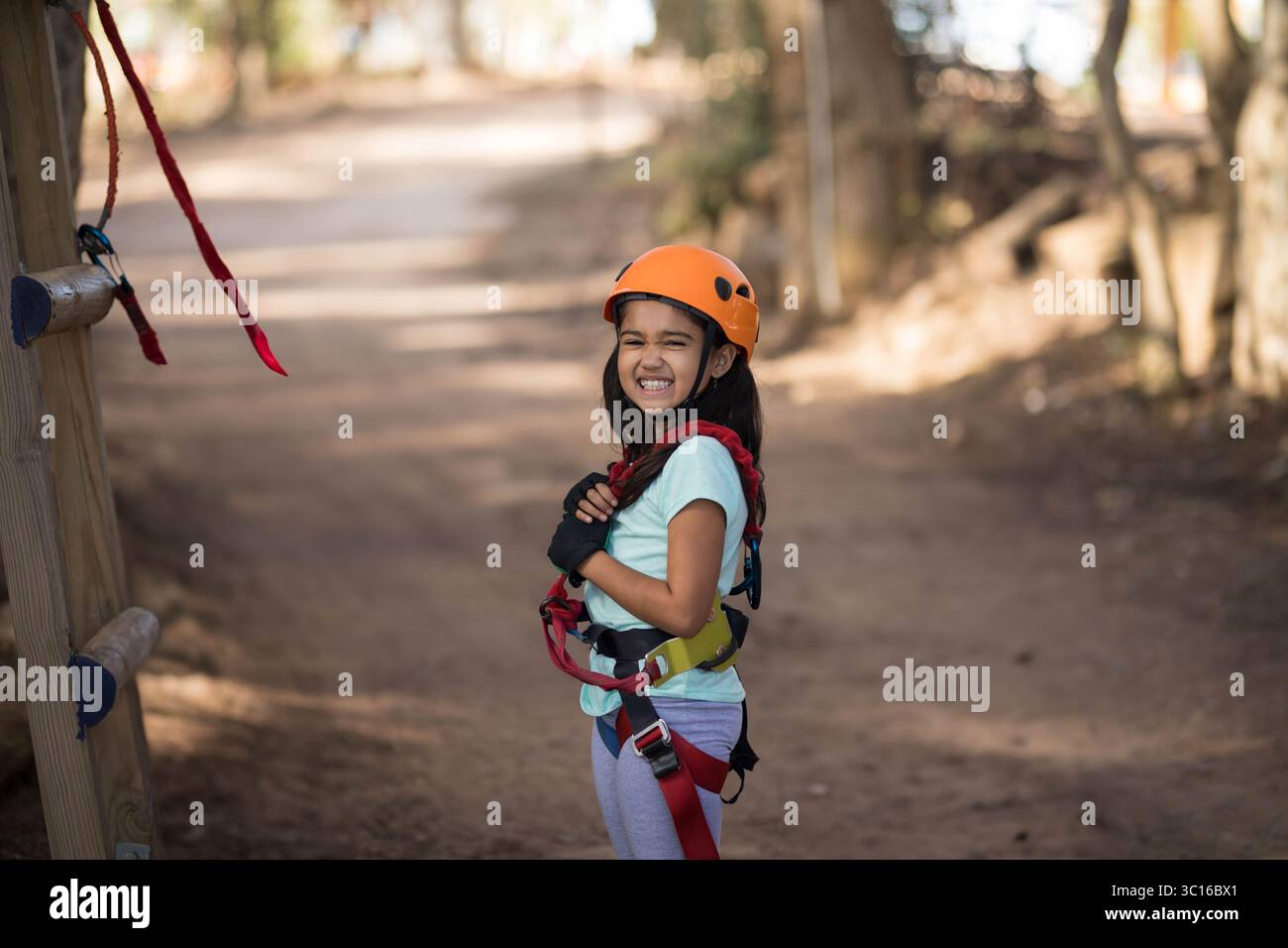 Girl Standing With Rope Asian girl standing next to climbing post wearing orange helmet and ...