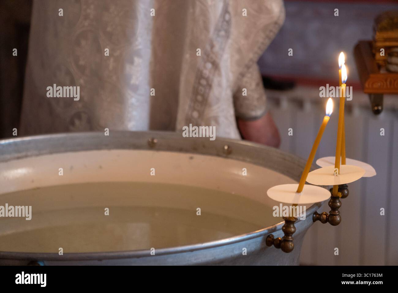 Close-up of a baptismal font filled with holy water and lit ceremonial ...