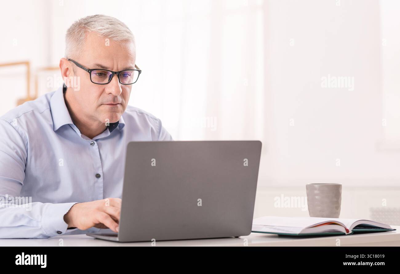 Serious senior man using laptop at office Stock Photo