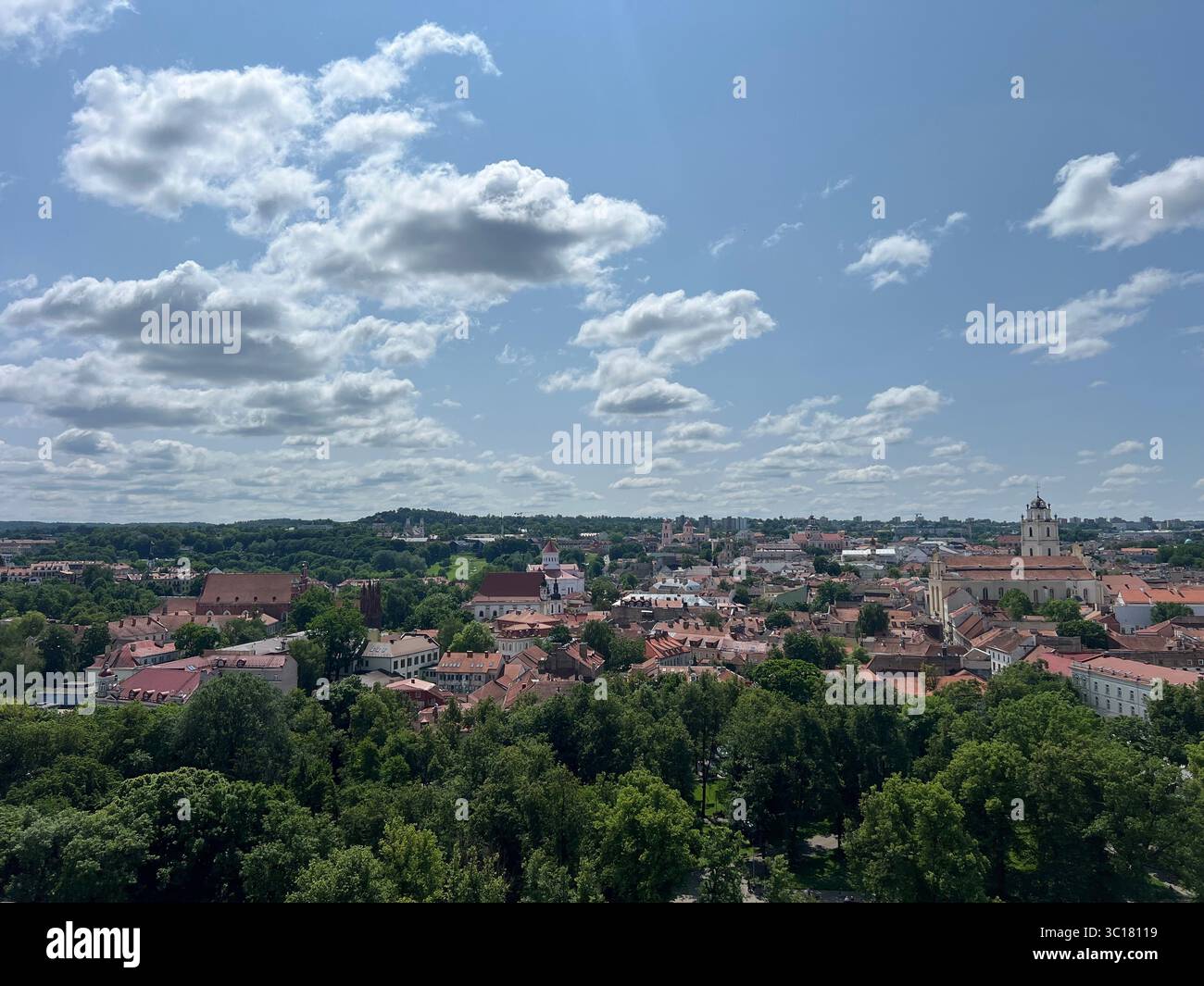 Panoramic summer view of Vilnius Old Town, Lithuania, from Gediminas Tower. Red rooftops, historic skyline, green trees, and blue sky with white cloud - Smartphone Captured Stock Image