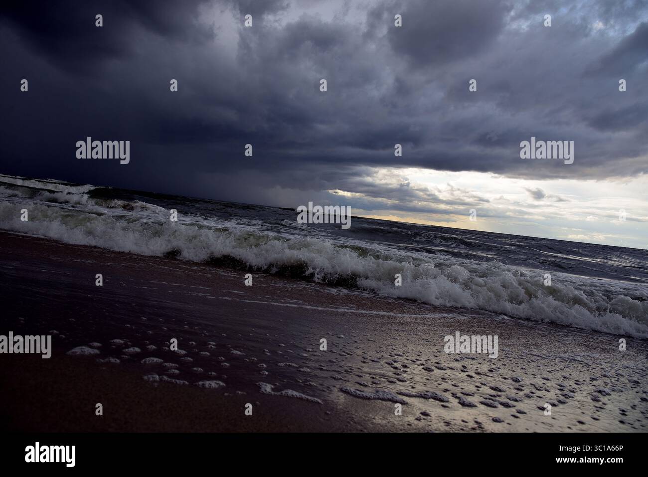 Dramatic seascape with dark storm clouds over the turbulent Baltic Sea on a sandy beach. Stock Photo