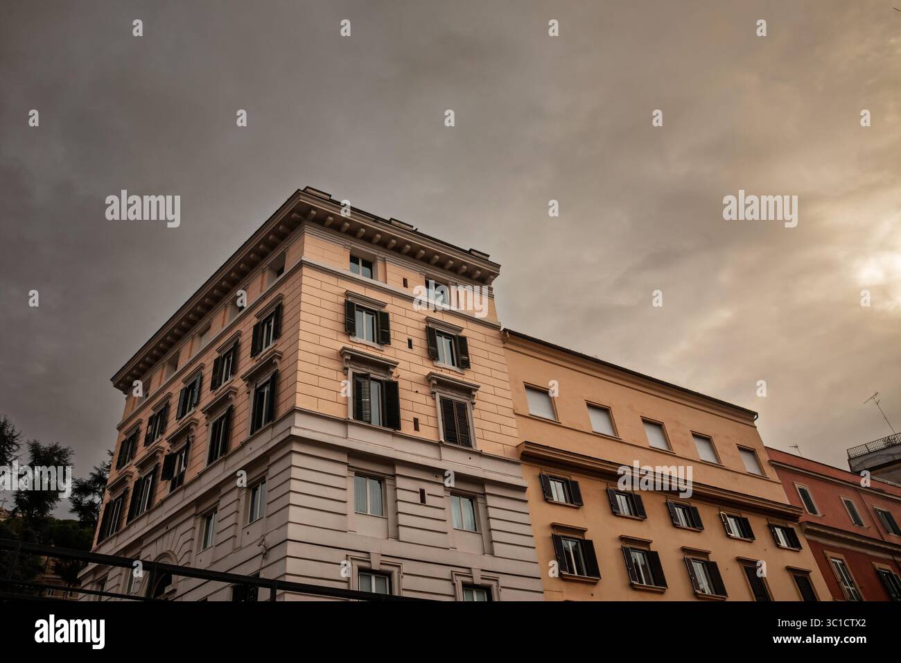 Oblique view of a late 19th‑century Roman apartment block with cream and ochre facades, shuttered windows and decorative cornices, silhouetted against Stock Photo
