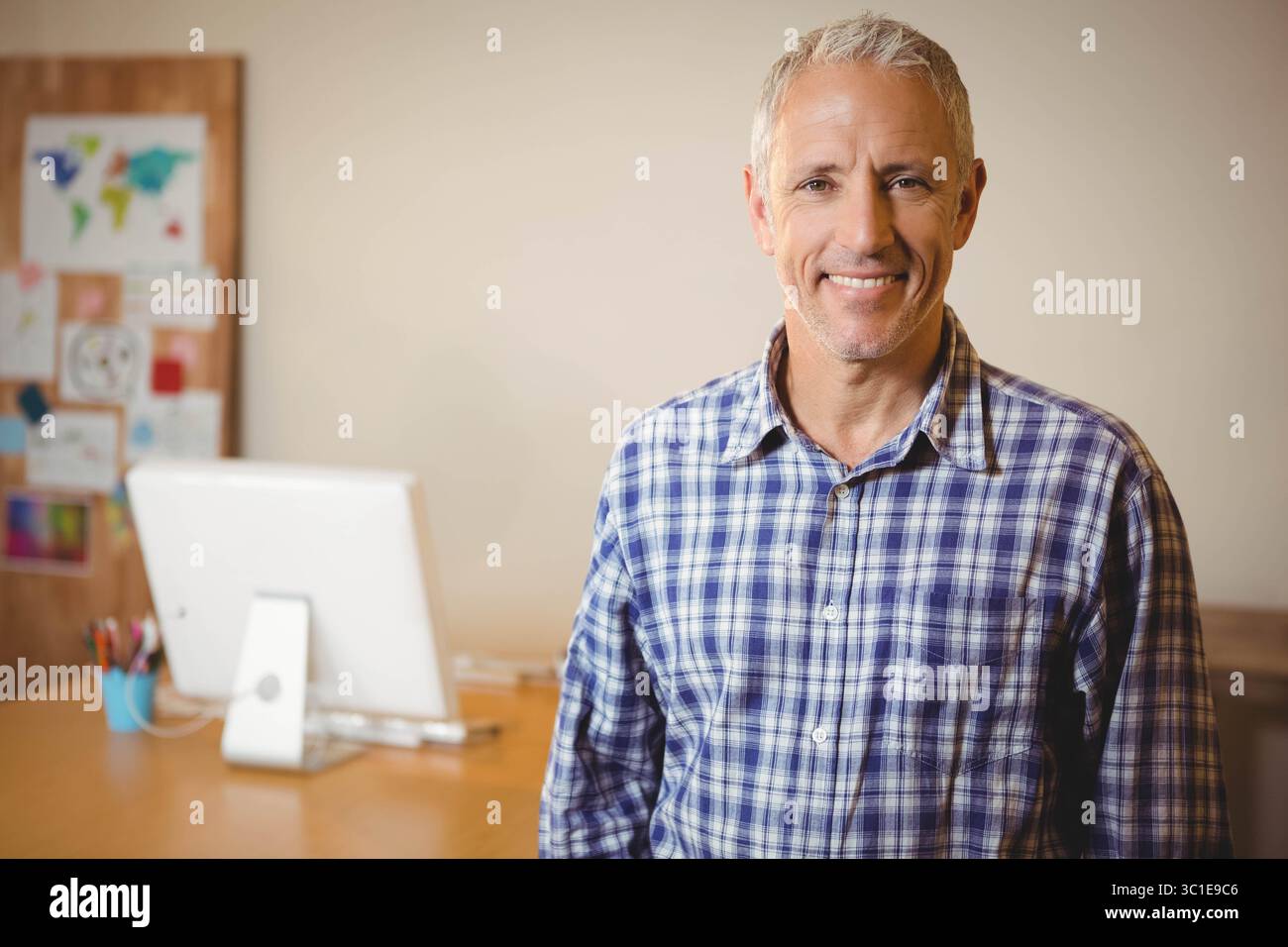 Man standing next to desk in home office, viewing computer monitor and ...