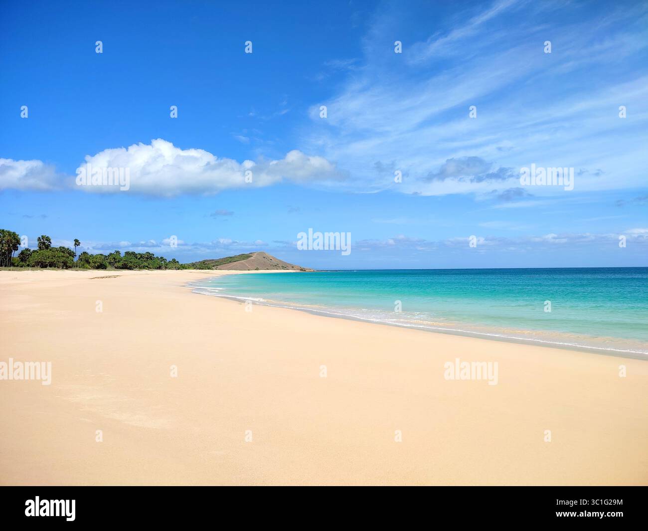Pristine tropical beach with soft golden sand, turquoise waters, and clear blue sky, surrounded by lush greenery and distant hills on a sunny day. - Smartphone Captured Stock Image