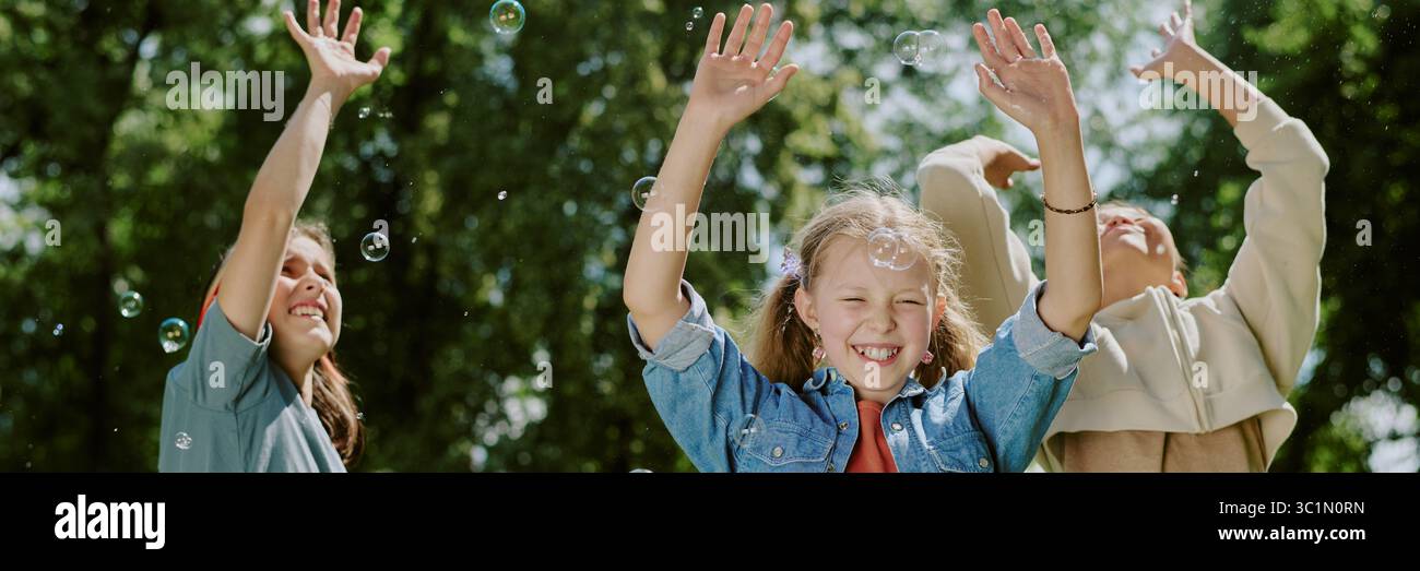 Children Laughing and Playing Outdoors with Bubbles in Park Stock Photo