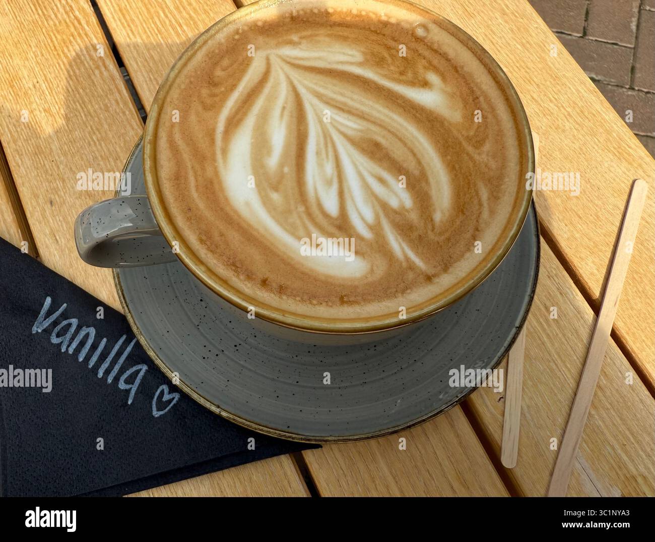 A cup of vanilla frothy coffee, latte, with a barista’s latte art pattern on top in a cafe - Smartphone Captured Stock Image