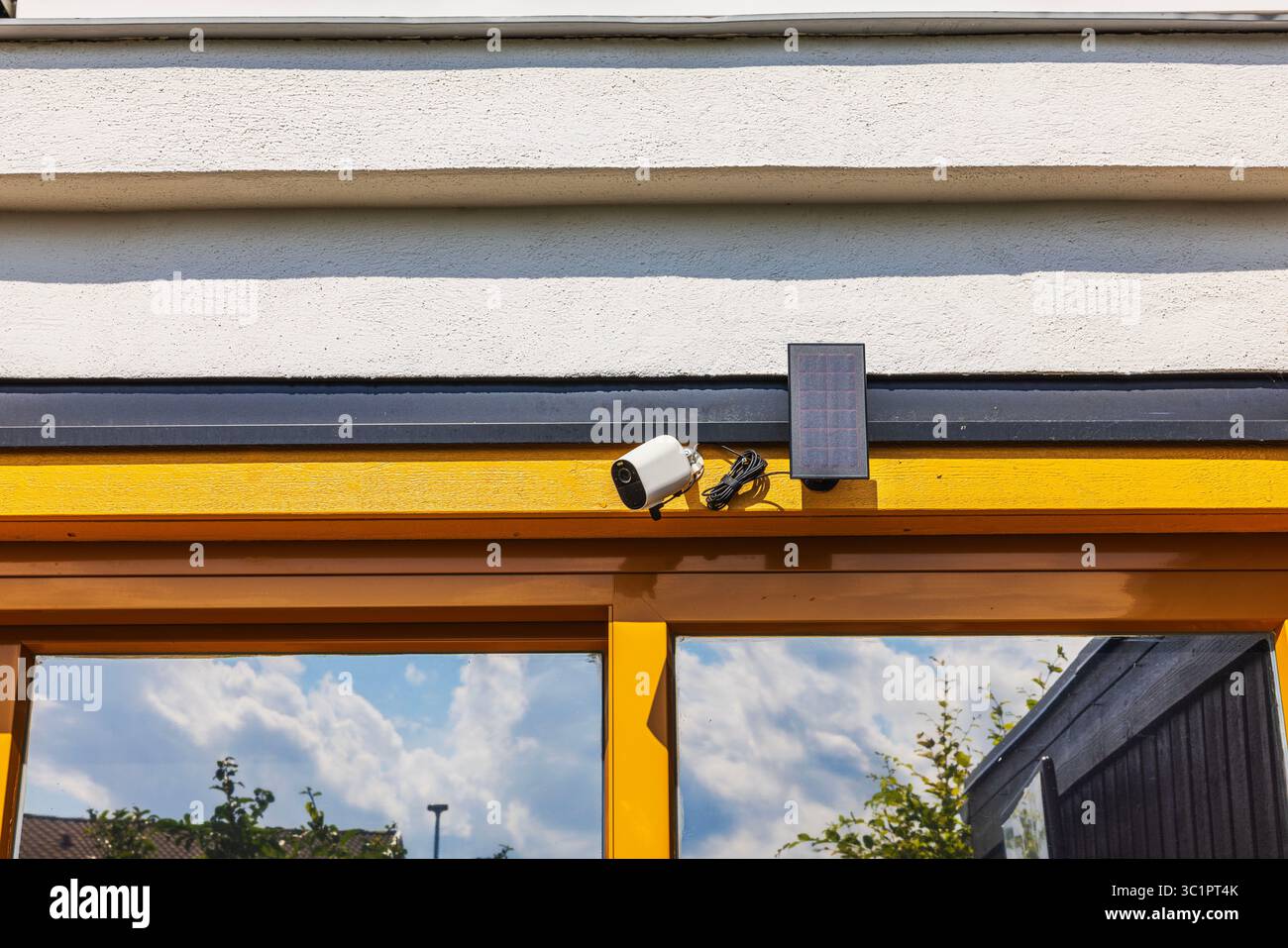 View of Security camera with solar panel mounted above yellow sliding windows ...