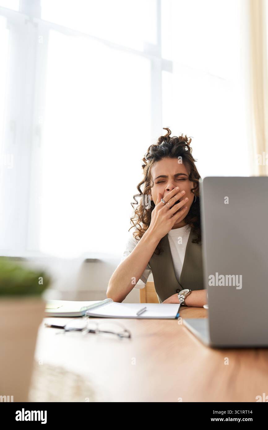 Curly-haired tired woman works from home at her desk, showing signs of ...