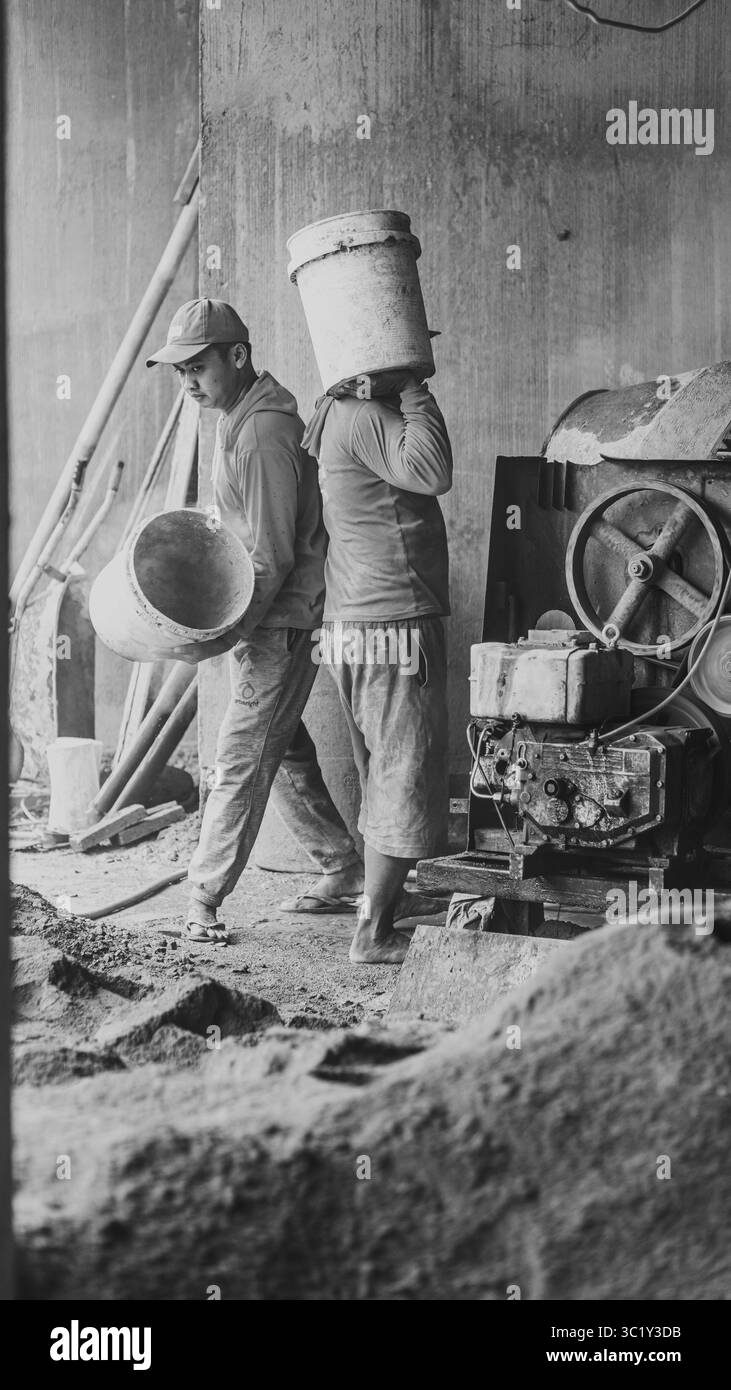 Construction workers collaborate in mixing cement, showcasing solid teamwork and efficiency in real on-site building operations. Stock Photo