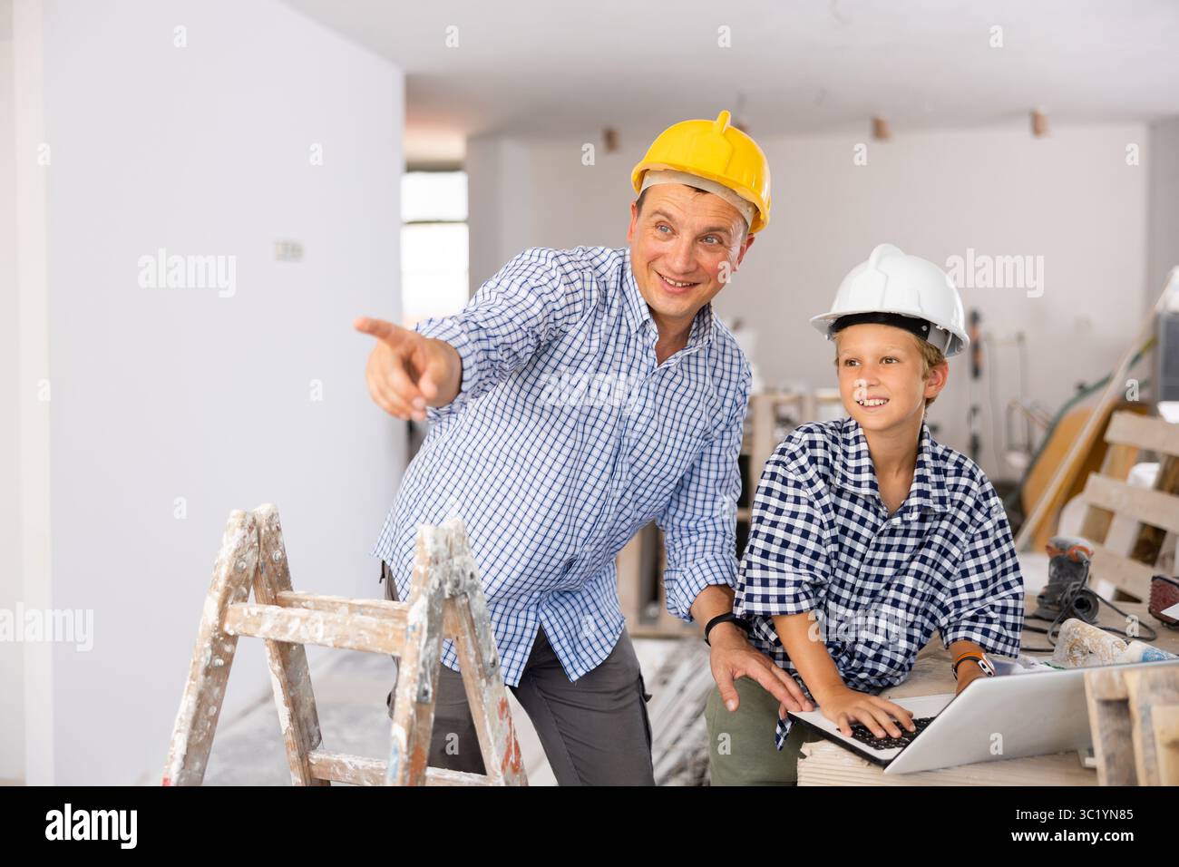 Man architect and boy using laptop while discussing working process in house being renovated Stock Photo