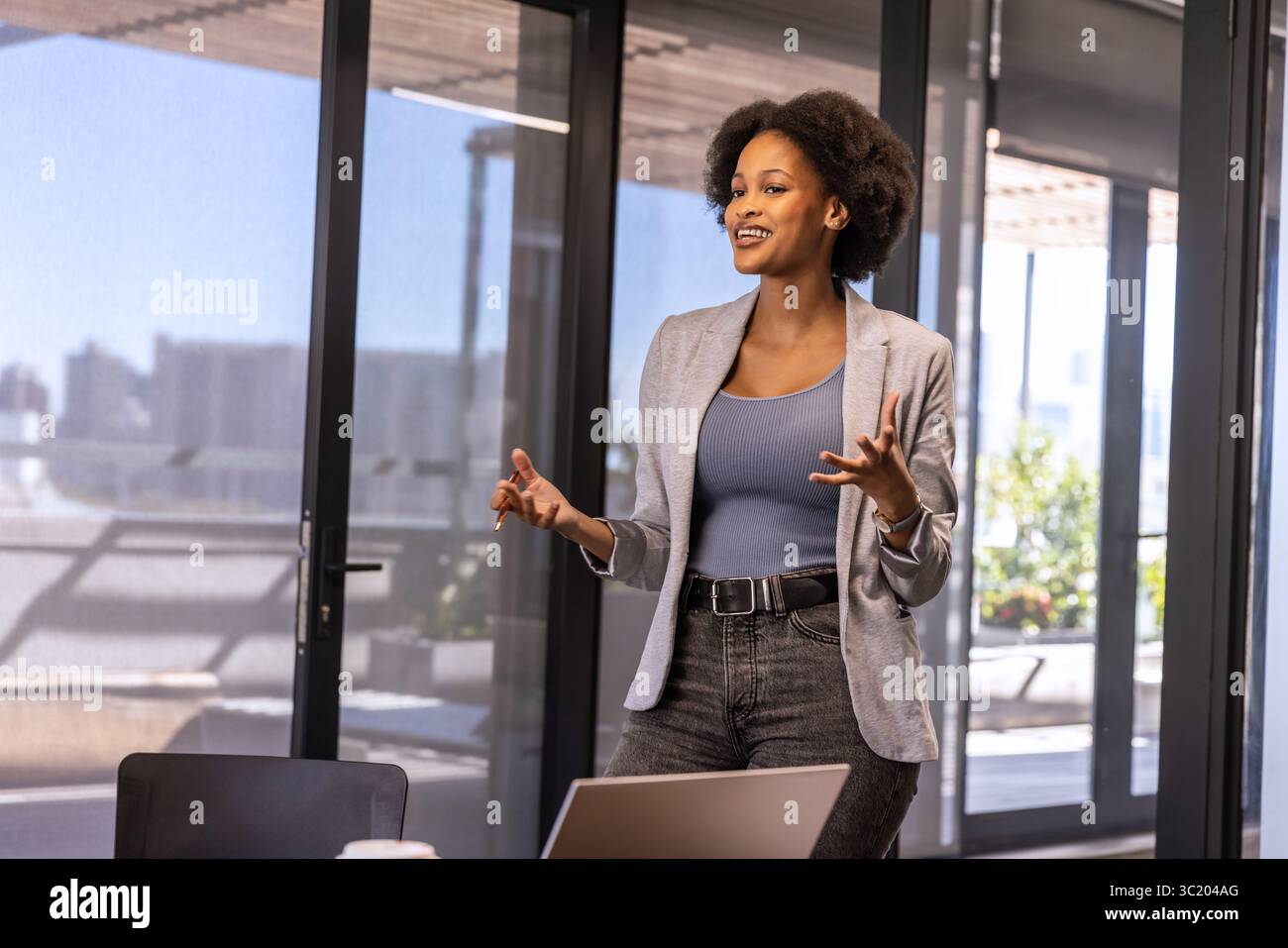 African American woman wearing blazer presenting at office table with laptop and plants, copy space Stock Photo
