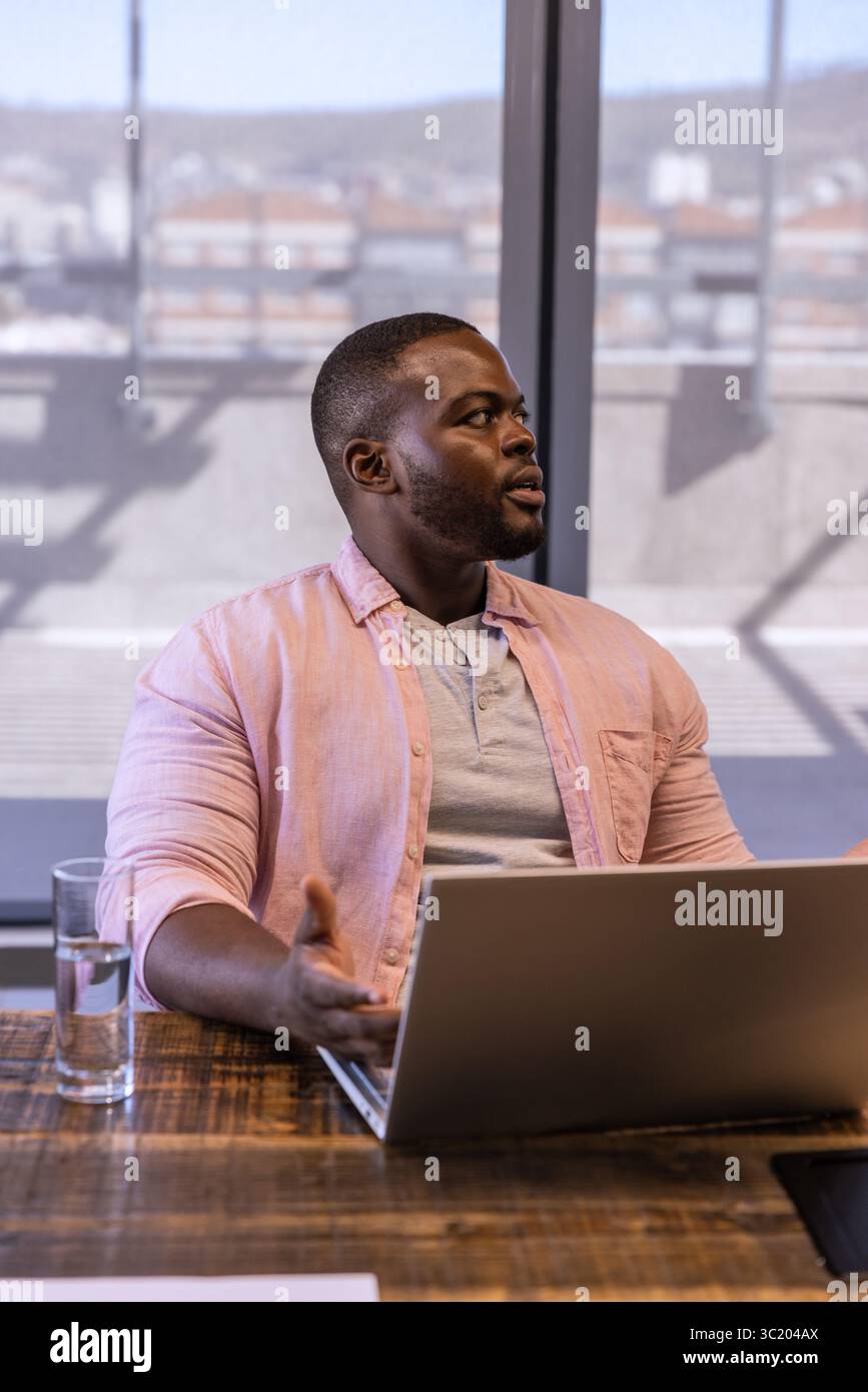 African American man gesturing during meeting at conference table with laptop, smartphone, water Stock Photo