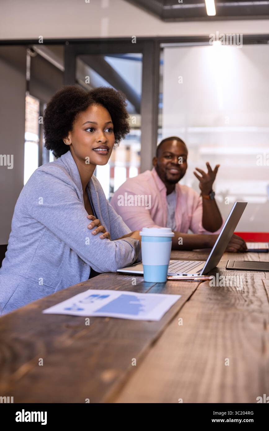 African American coworkers in business attire analyzing chart on table with laptop in meeting room Stock Photo