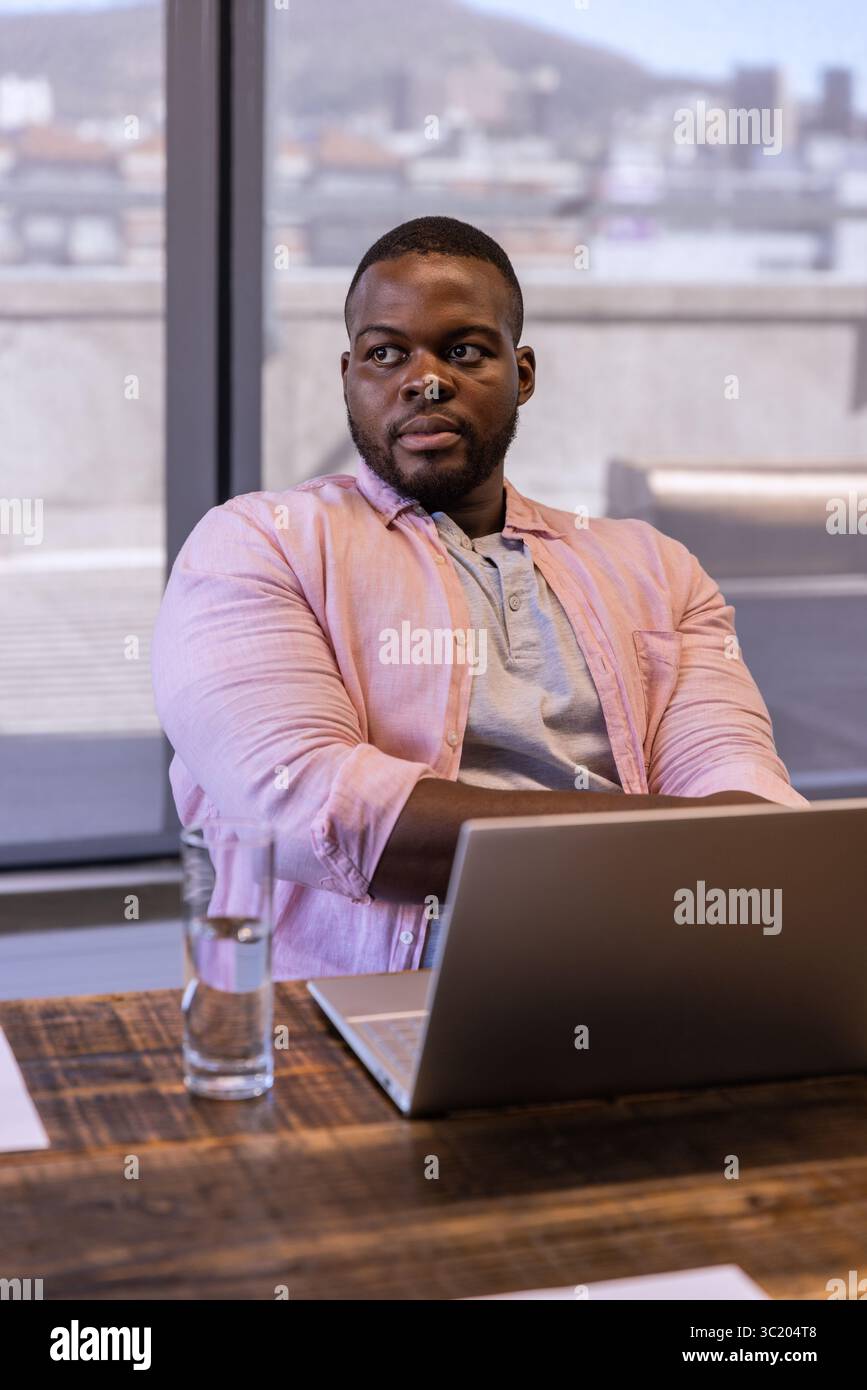 African American man sitting at office table folding arms over laptop wearing business attire Stock Photo